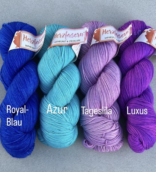 Das Bild zeigt vier Stränge handgefärbte Wolle von Herzfasern No. 11, nebeneinander gelegt. Von links nach rechts: ein kräftiges Royalblau, ein leuchtendes Azurblau, ein zartes Tageslila und ein sattes, kräftiges Violett mit dem Namen Luxus. Alle Stränge 